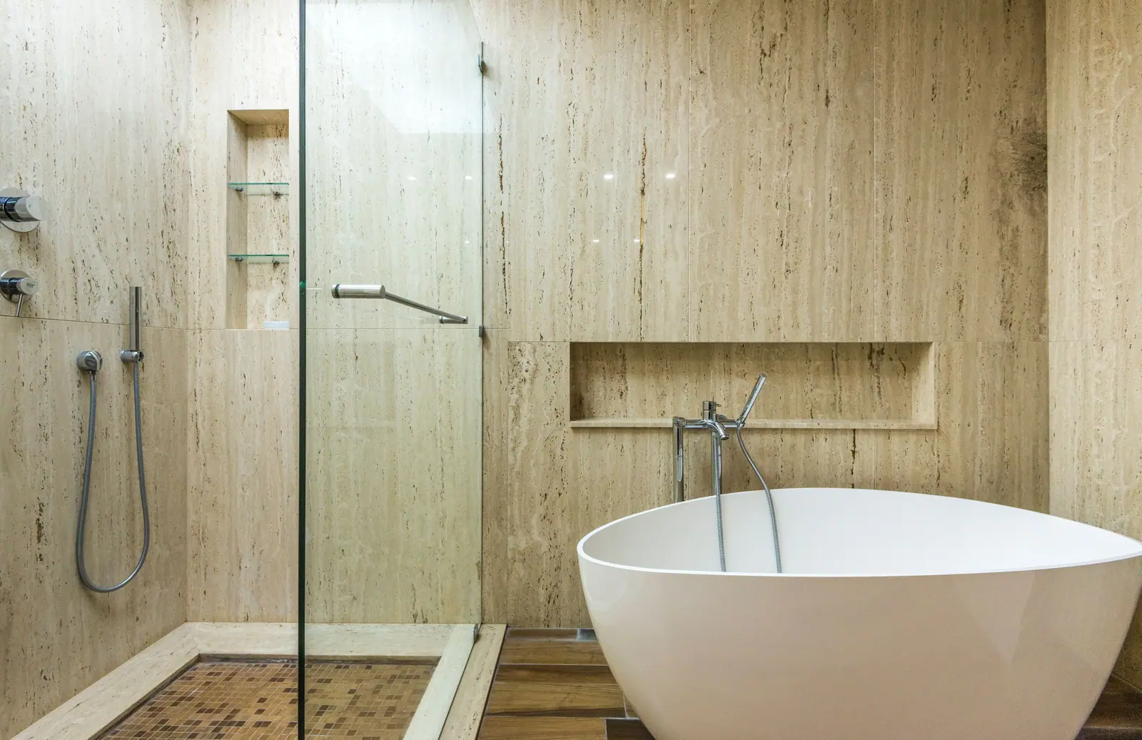 A travertine bathroom with a walk-in glass shower and a freestanding tub