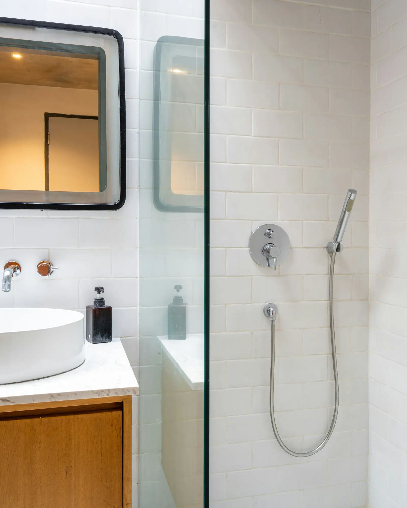 A white tiled bathroom with a round basin on a teak vanity