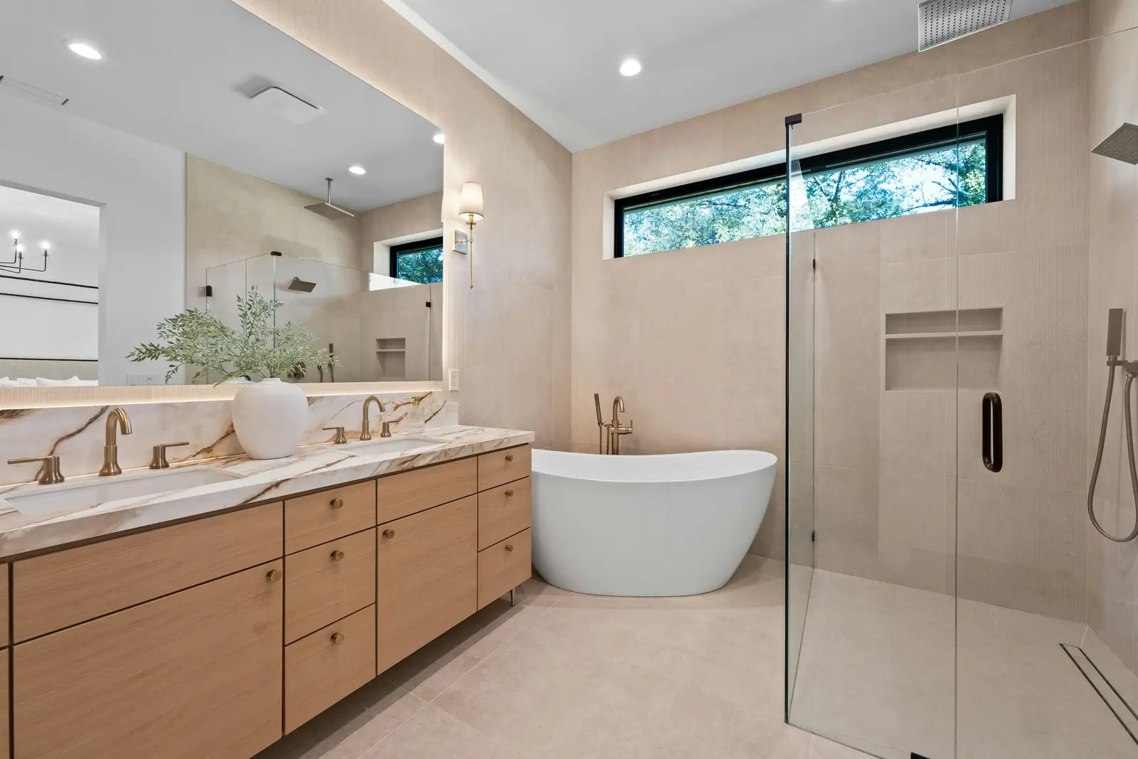 A bright bathroom with an oak double vanity, marble counter and freestanding tub