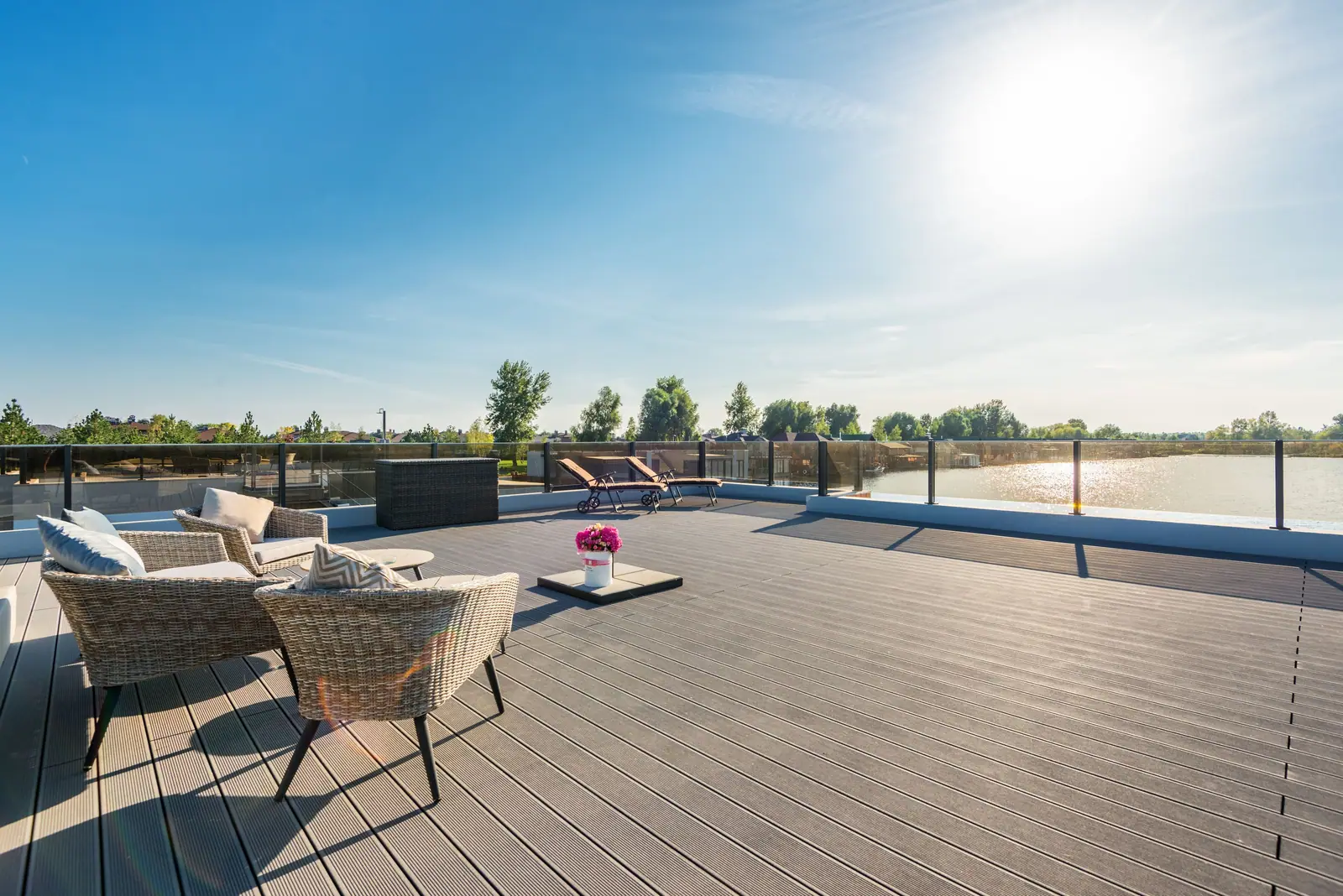 Wicker armchairs and a low table on a sunlit deck above calm water