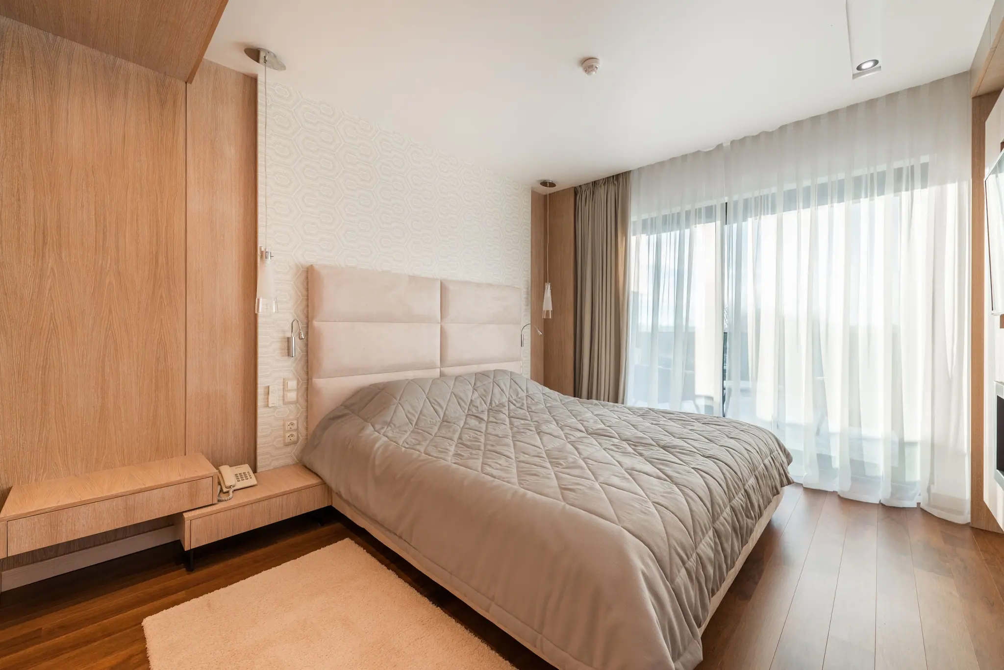 The Junior Suite bedroom: an upholstered headboard, oak panelling and sheer curtains