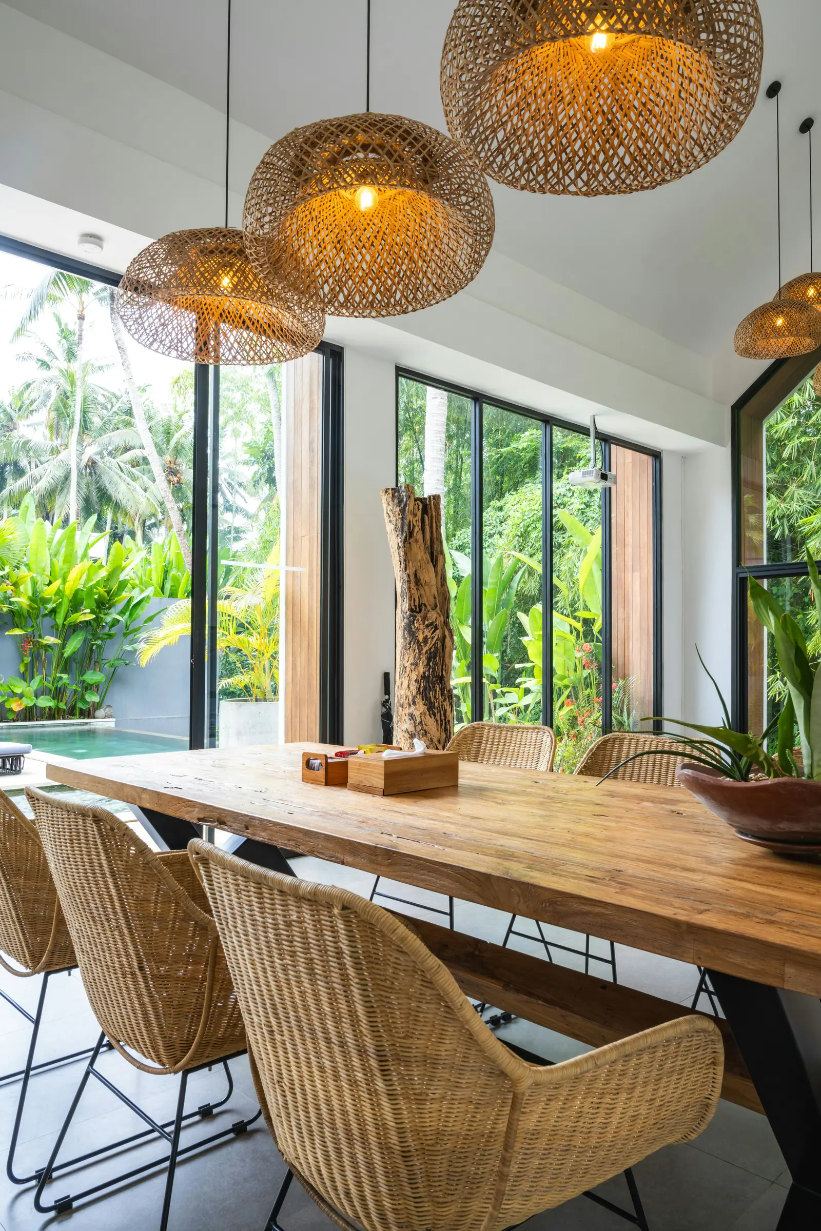 The dining room: a long timber table with woven chairs under rattan pendants